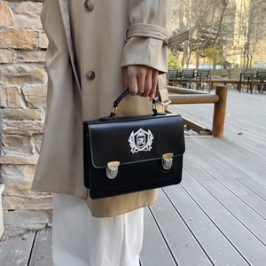 Vintage black leather satchel bag with crest embroidery shown in an outdoor setting