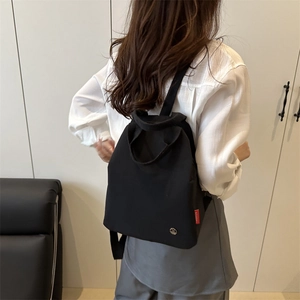Minimalist black canvas backpack with adjustable straps and logo detail shown on model