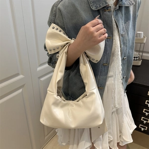 Chic cream white bow shoulder bag with silver rivets and glossy finish on a female model