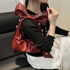 Red bow shoulder bag with silver studs and glossy finish shown on model in white dress