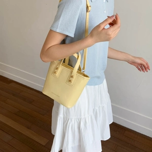 Detail of light yellow mini bucket bag with fashion & bags text and golden rivets