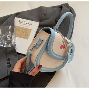 Détail du sac selle blanc et bleu avec imprimé cerises et poignée chaîne décorative