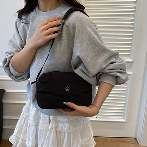 Minimalist black nylon crossbody bag with wide shoulder strap and circular metal logo
