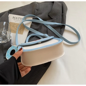 Détail du sac selle bleu et crème avec charm donut et texture en cuir mat