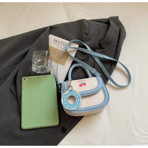 Détail du sac selle bleu clair avec imprimé cerise et breloque donut sur blazer gris