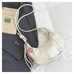 Detail of cream croissant bag featuring knotted strap and heart-shaped pendant accessory