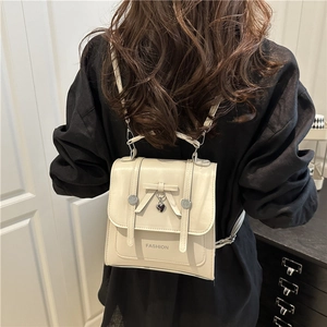Preppy cream leather backpack with bow and heart charm worn by model in home setting