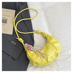 Detail of yellow hobo bag with pink heart charm and braided tassel on a grey blazer