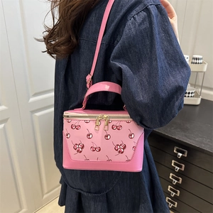 Pink cherry print crossbody box bag with top handle and golden zippers worn by model