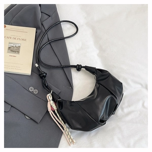 Detail of black pleated croissant bag with glossy finish and braided rope pendant