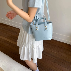 Elegant light blue bucket bag with gold hardware shown as a crossbody by female model