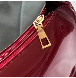 Detail of a dark red patent leather bag with a sleek gold zipper and metallic finish
