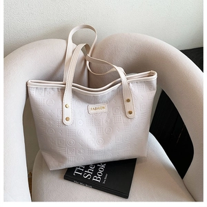 Gros plan des motifs gaufrés et du logo doré sur un sac fourre-tout de couleur crème