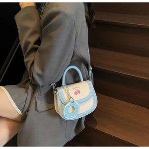 Détail du sac selle blanc et bleu avec motif cerise et breloque beignet sucré