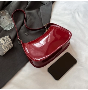 Dark red patent leather underarm bag shown next to a smartphone for size reference