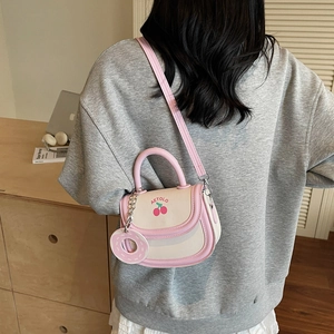Sac selle rose et beige avec broderie cerise et breloque donut dans un cadre naturel doux