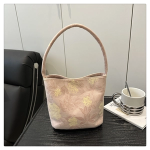 Détail de broderie florale sur un sac seau en tissu rose clair avec poignée souple