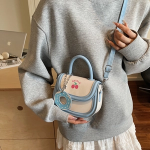 Sacoche bleu et blanc avec motif cerise et breloque donut portée par un mannequin en tenue