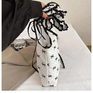 Detailed side view of white polka dot canvas tote bag with black ruffle edge and bow