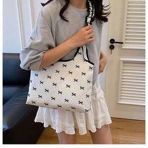 Chic tote bag with black bow prints and stylish ruffled strap shown in a home setting
