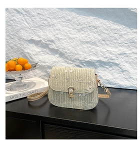 Detail view of woven straw bag featuring delicate white flower embroidery and metal buckle