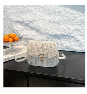 Close-up of woven straw saddle bag featuring floral embroidery and gold metal clasp