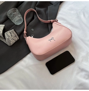 Detailed view of pink leather baguette bag with silver bow accent on bedsheets