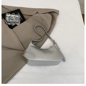 Detail view of crescent silver metallic shoulder bag on a minimalist white background