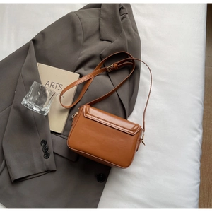 Detailansicht braune Leder-Umhängetasche mit goldener Hardware auf einem Blazer-Hintergrund