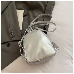 Detail of silver metallic mini backpack on white cloth and grey blazer background