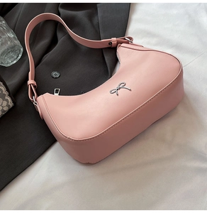 Detail of pink leather hobo bag with a silver metal bow logo and matching shoulder strap