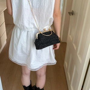 Detail of a vintage-style black woven clutch bag with gold chain strap on a model