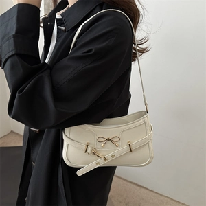 Creamy white PU leather underarm bag with metal bow detail worn over a black coat