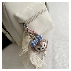 Close-up of a plush bear charm with lace ribbon attached to a white student backpack