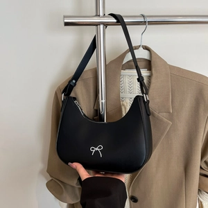 Detail of black crescent shoulder bag featuring a silver bow accent and leather texture