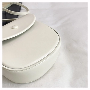 Detailed macro view of the cream saddle bag showing precision stitching and decorative buckle