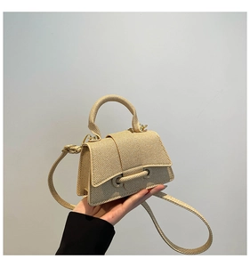 Detail of hand-held beige woven trapezoid handbag with textured finish and strap
