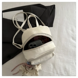 Inside view of an off-white mini backpack holding a phone and cards on a bed
