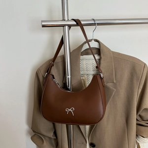 Detail of a brown shoulder bag with a silver bow decoration and adjustable strap buckle