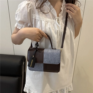 Chic color-block handbag with brown leather and grey denim panels on a white lace dress