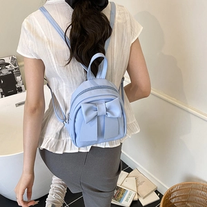 Light blue mini backpack with large bow detail and adjustable straps on a female model