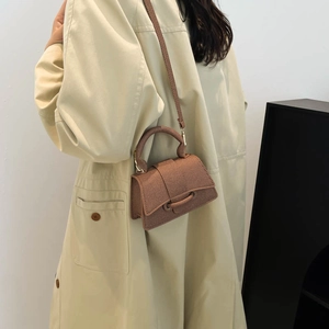 Brown textured mini handbag with circular handle and crossbody strap on a beige trench coat