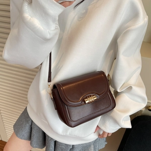 Elegante dunkelbraune rechteckige Umhängetasche mit goldener Schließe über weißem Pullover