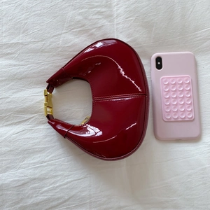 Détail du sac demi-lune en cuir verni bordeaux avec garniture dorée et comparatif