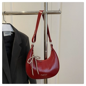 Détail du sac croissant rouge en cuir verni brillant avec pendentif nœud perlé