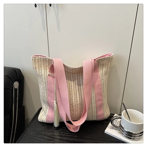 Detail of hand-woven straw tote bag with pink canvas handles and tassel charm on wood table