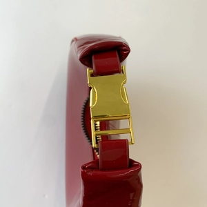 Détail du sac en cuir verni rouge montrant la boucle dorée et la finition brillante