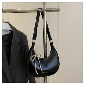 Détail du sac croissant en cuir verni noir brillant orné d'un nœud décoratif en perles
