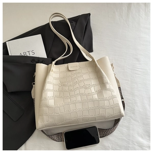 Detail of creamy white tote bag featuring crocodile embossed texture and wide woven strap