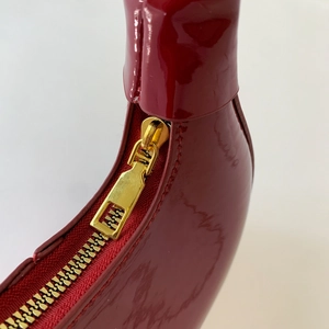 Détail de la fermeture éclair dorée sur un sac à main en cuir verni rouge vin